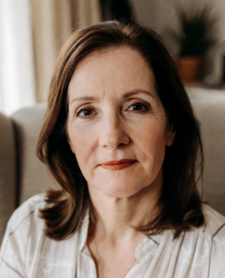 Femme d’environ assise dans un fauteuil cosy chez elle, évoquant le calme et l’introspection nécessaires pour travailler sur les causes énergétiques du cancer du sein